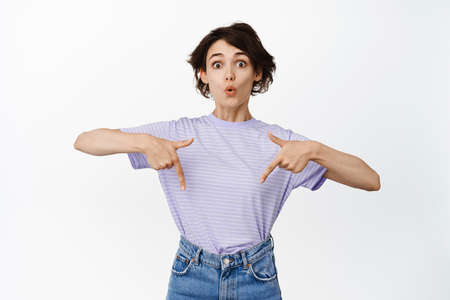 Wow look down. Intrigued brunette girl with short hairstyle, pointing fingers below and showing sale...