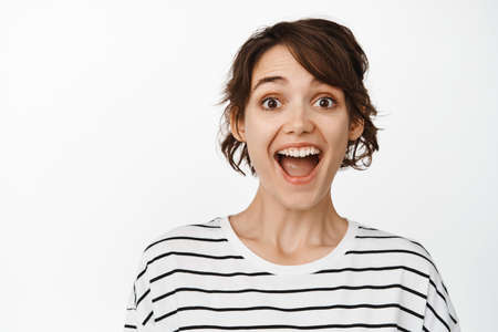 Close up portrait of surprised and amazed brunette woman, gasping fascinated, looking astonished, standing against white backgroundの写真素材