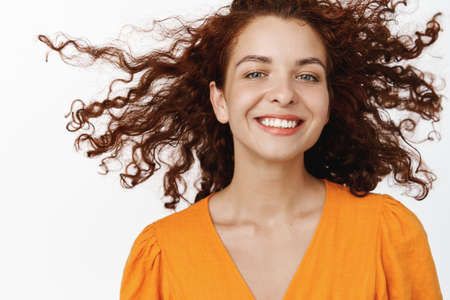 Skin care and haircare cosmetics. Beautiful smiling woman with curly red hair flying in air,...