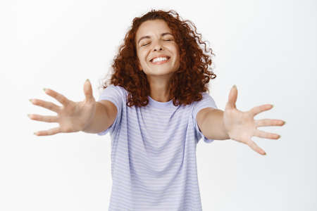 Image of carefree young woman reaching with hands, stretching out arms and smiling with eyes closed,...
