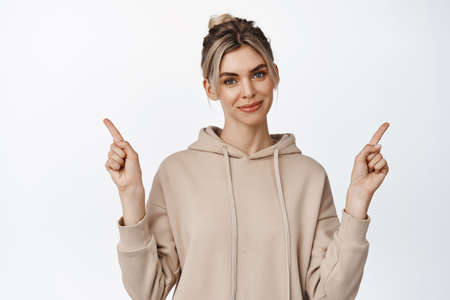 Portrait of attractive smiling woman pointing sideways, showing two options, both ways, standing against white backgroundの写真素材