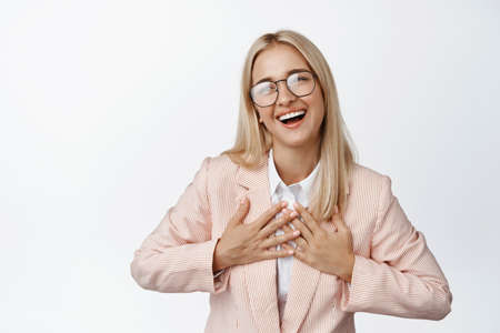 Young female entrepreneur say thank you, holding hands on chest and smiling, standing in suit and glasses against white backgroundの写真素材