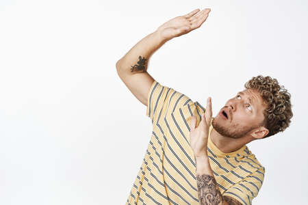 Scared guy defending himself from something falling from above, bending and stretching out hands in protection, standing over white backgroundの写真素材