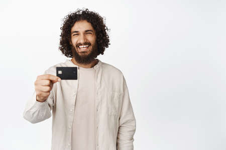 Happy smiling hispanic man showing credit card, looking satisfied, recommending bank, white...