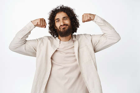 Image of handsome hispanic macho man, showing biceps, flexing muscles and looking cool, smiling...