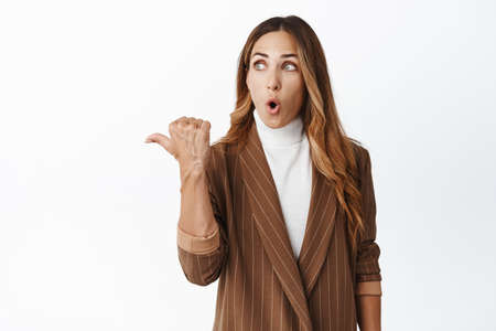 Business concept. Amazed businesswoman pointing and looking left, saying wow at product advertisement, showing empty space, white backgroundの写真素材