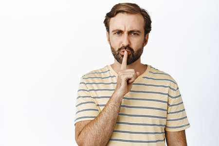 Portrait of angry man shushing and looking displeased, tell to be quiet, scolding loud person, shut up gesture, standing over white backgroundの写真素材