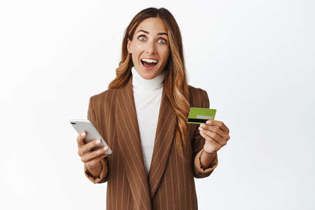 Online shopping. Amazed middle aged woman using credit card and mobile phone app, smiling excited...