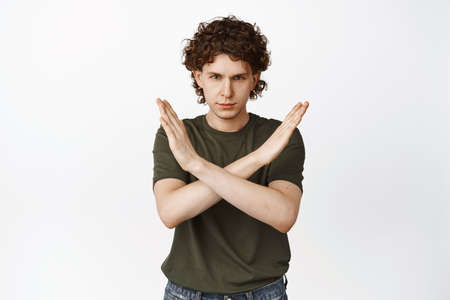 Serious and confident curly man making cross gesture, prohibit smth, disagree, rejecting offer,...