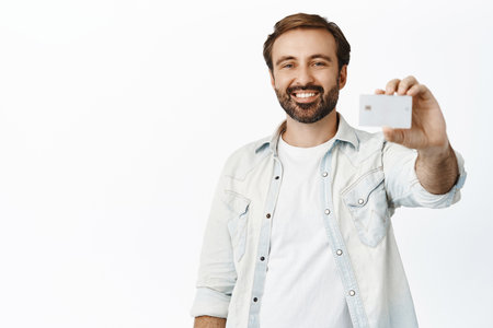 Smiling handsome man showing credit card with pleased face, client recommending bank or store, white backgroundの写真素材