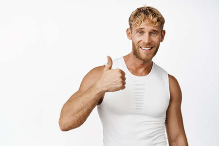Smiling sportsman showing thumbs up in approval, fitness athlete gives permission, praise and compliment, white backgroundの写真素材
