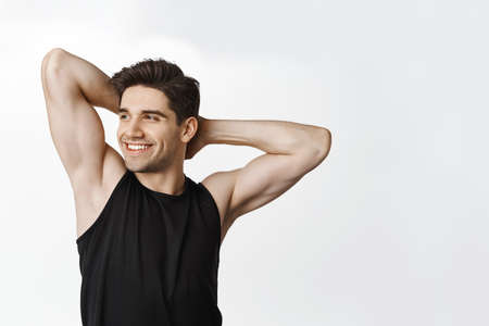 Handsome athletic man with fit strong body, biceps, holding hands behind head, show off his muscles and smiling pleased, concept of gym workout and healthの写真素材