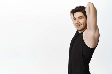 Profile portrait of male athlete, fitness guy stretching arms behind back, warm up before workout exercises, smiling happy at cameraの写真素材
