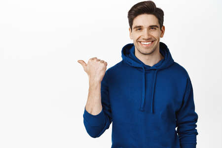 Handsome smiling brunette guy pointing left, wearing casual clothes, showing advertisement on blank empty space, white backgroundの写真素材