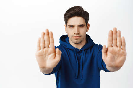 Stop, back off. Serious brunette guy extends palms at camera, telling no, prohibit smth bad, standing over white backgroundの写真素材