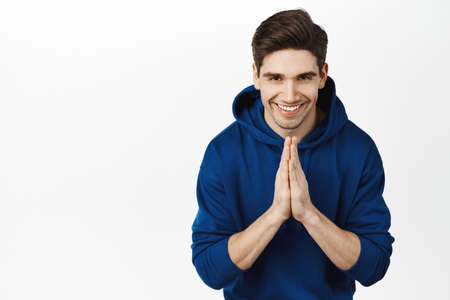 Namaste. Smiling young man bowing with hands clasped together, greeting sensei, express gratitude, standing in hoodie over white backgroundの写真素材