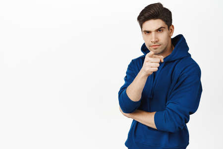 Suspicious man with frowned face, pointing finger at camera and looks serious at camera, stands over white backgroundの写真素材