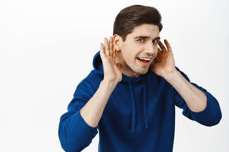 Portrait of eavesdropping guy bending closer and holding hands near ear, cant hear you, overhear...