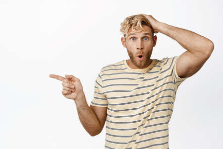 Portrait of blond guy looking surprised, pointing left at promo sale, white backgroundの写真素材