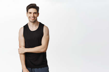 Sport and workout. Handsome smiling man posing in tank top against white studio backgroundの写真素材
