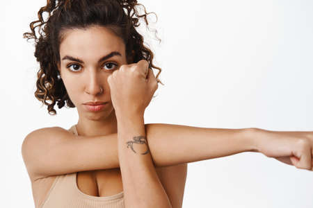 Close up of fitness girl, young female athlete workout, stretching arms, warm up in gym before exercises, standing in sportswear against white backgroundの写真素材