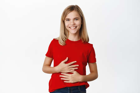 Smiling satisfied cute little girl, rubbing her belly stomach and looking pleased, eating well,...