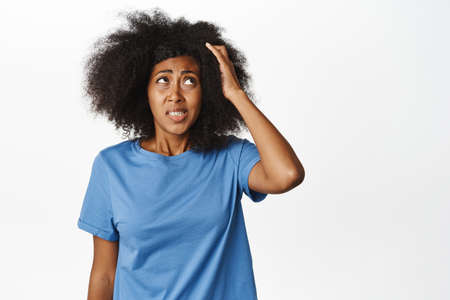 Confused african american woman scratching head and looking clueless, puzzled to answer, standing in blue t-shirt over white backgroundの写真素材