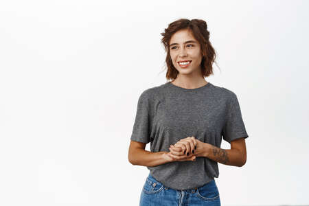Young smiling brunette woman holds hands together, looking friendly and assertive, help client,...