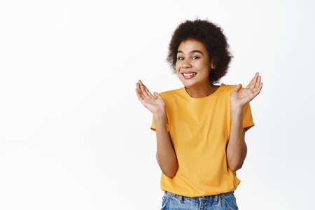 Oops. Smiling silly black girl showing shrugging pose and looking guilty, standing in yellow tshirt...