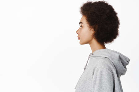 Profile of young modern african girl with afro curly hair, looking left at copy space with casual normal face expression, standing over white backgroundの写真素材