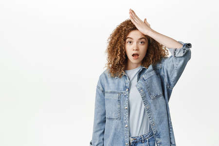 Portrait of shocked and troubled woman facepalm, looking alarmed and worried, remember or forgot smth, standing over white backgroundの写真素材