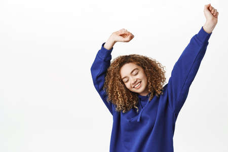 Happy smiling girl holding empty space, raising arms up and with cheerful face expression, standing...