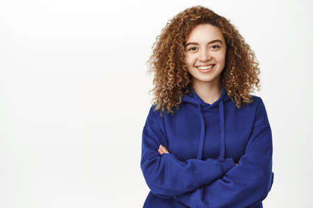 Close up portrait of happy young beautiful woman, smiling and looking confident, cross arms on chest, relaxed and natural, standing against white backgroundの写真素材