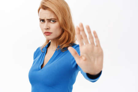 Portrait of girl extending her palm, saying no, dislike smth, prohibit, rejecting offer, standing over white backgroundの写真素材