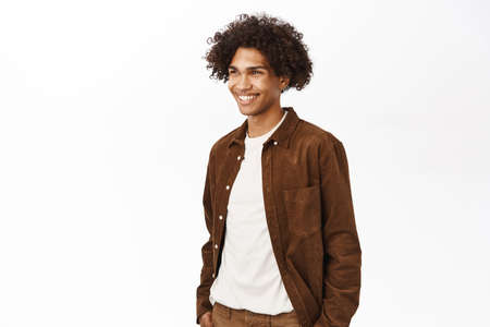 Portrait of smiling hispanic man with confident face, holding hands in pockets, standing casually against white backgroundの写真素材