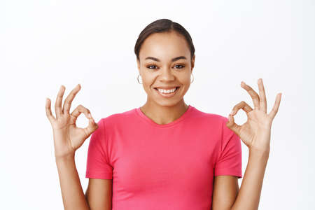 Close up of smiling black woman shows okay sign, say yes, approves smth, recommends product or...