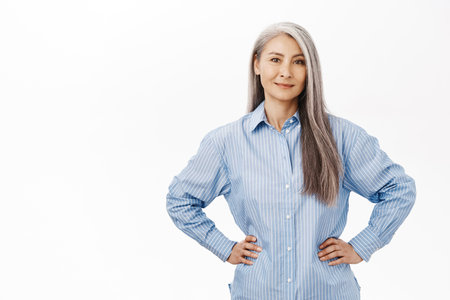 Smiling asian lady, senior korean woman, looking confident, standing against white background