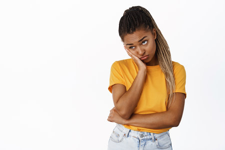 Bored and sad Black girl roll eyes, facepalm and stare tired aside, standing in yellow t-shirt over white backgroundの写真素材