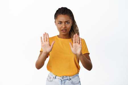 Serious and concerned Black woman showing stop, no rejection gesture, refusing smth, tell to stop, frowning at camera, standing over white backgroundの写真素材
