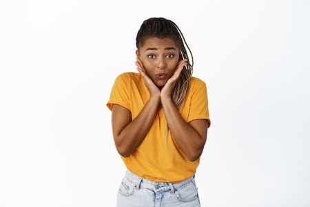 Image of excited and surprised Black girl looking with interest and amusement, anticipating something, standing over white backgroundの写真素材