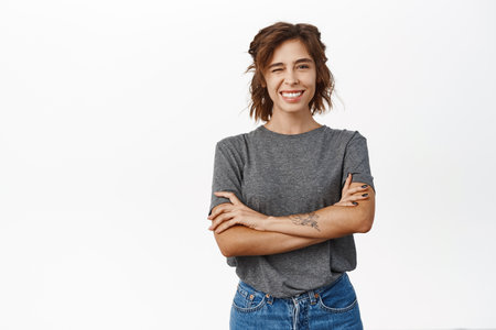 Happy smiling young hispanic woman, wearing grey t-shirt, looking cheerful, standing confident against white backgroundの写真素材