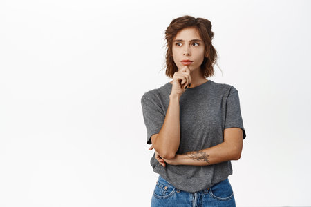 Woman with thoughtful face touching chin, thinking, making decision, standing in grey tshirt over white backgroundの写真素材
