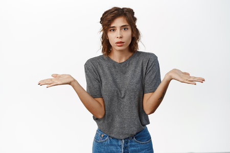 Confused young woman shrugging shoulders, looking puzzled, dont know, standing puzzled against white backgroundの写真素材