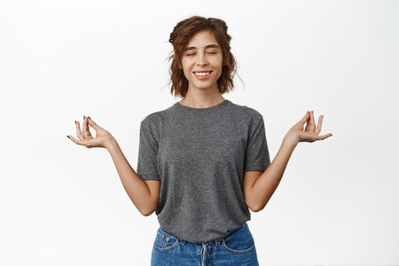 Peace and zen, smiling young woman meditating, using meditation app, close eyes, standing relaxed, white backgroundの写真素材