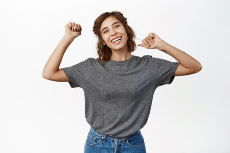 Portrait of beautiful happy girl smiling and dancing with raised arms, having fun, posing pleased against white backgroundの写真素材