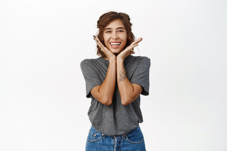 Adorable young woman with perfect facial skin without makeup, smiling white teeth, showing her face and laughing satisfied, standing over white backgroundの写真素材