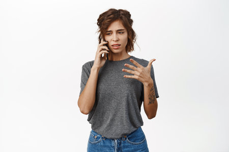 Worried woman talks on mobile phone. Upset girl has cellphone call conversation, stands over white backgroundの写真素材
