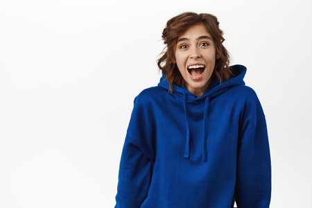 Portrait of young beautiful girl showing reaction of surprise, staring amazed at camera, checking out smth awesome, standing over white backgroundの写真素材