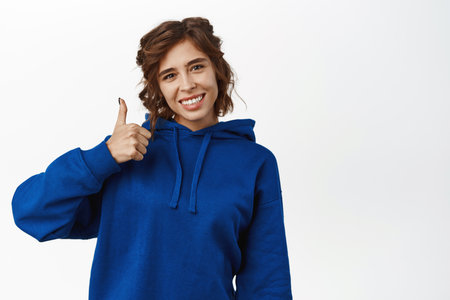 Very good. Smiling brunette woman showing thumbs up, good job gesture, like and recommend store, complimenting, standing in casual clothes over white backgroundの写真素材