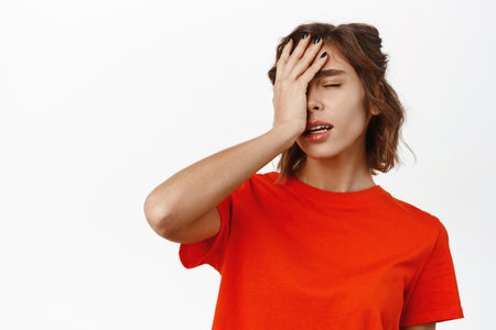 Facepalm girl. Disappointed young woman looking tired, slap face with hand, standing distressed and upset, white studio backgroundの写真素材